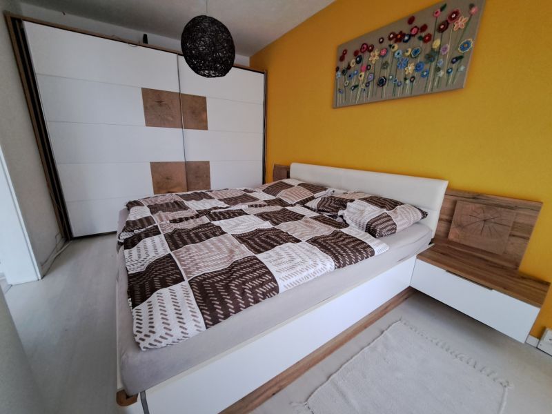 A bedroom in a three-room apartment with a bed, a large wardrobe, and a yellow wall.