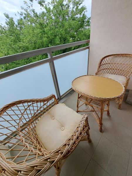 A balcony of a 3-room apartment with chairs and a table, green trees in the background.
