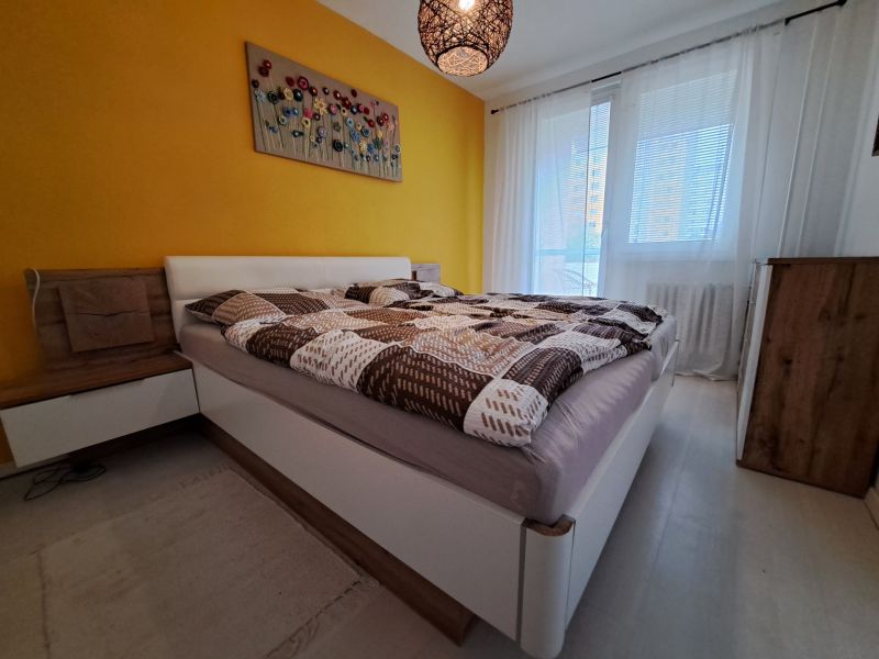 A bedroom in a 3-room apartment with white curtains and a yellow wall, and a floor with a wooden decor.