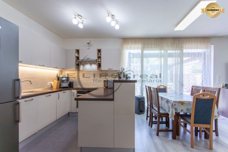 A kitchen with white cabinets, a dining table, a wooden decor floor, bright windows.