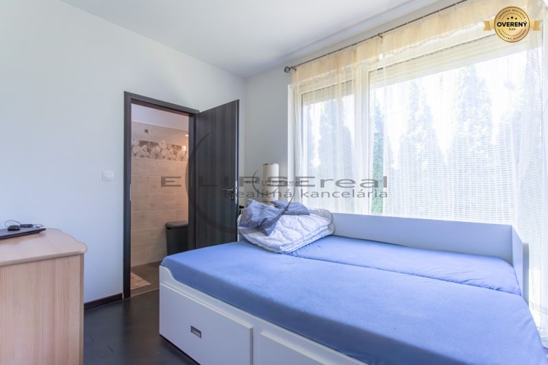 A room in a family house with a bed, a dresser, and large windows.
