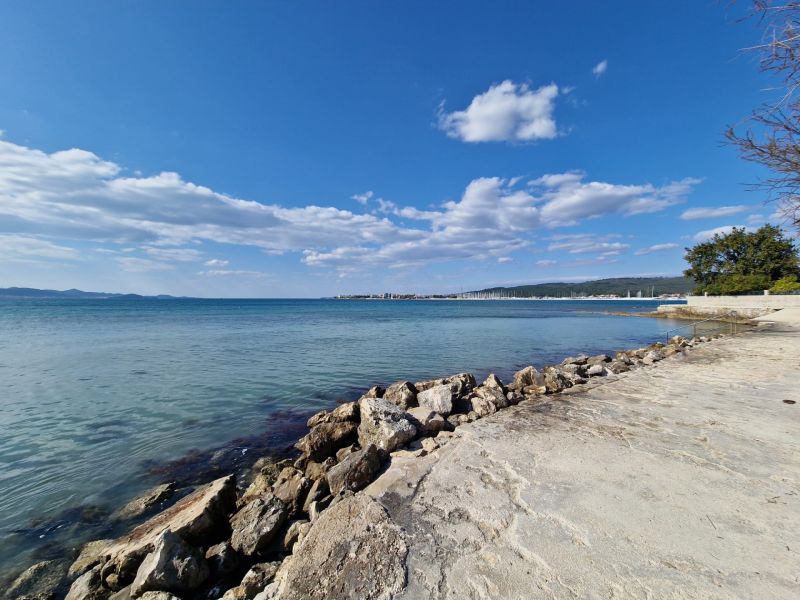 The coast in Sukošan with clear water and a rocky shore under a blue sky.