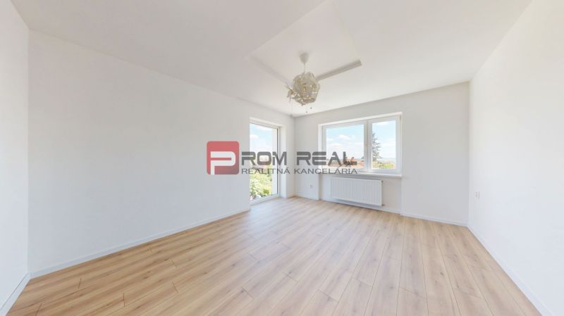 Bright empty interior with wood-decor flooring, large windows, and white walls in a family house.