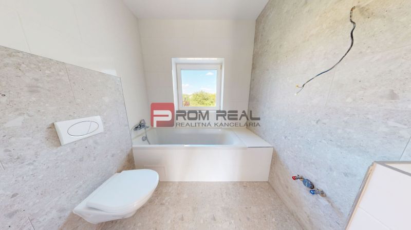 A bathroom in a family house with a bathtub, a window, and light-colored tiles on the walls and floor.