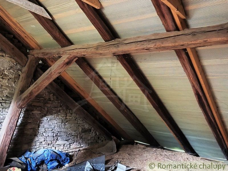 The attic of the cottage with wooden beams and a stone wall.