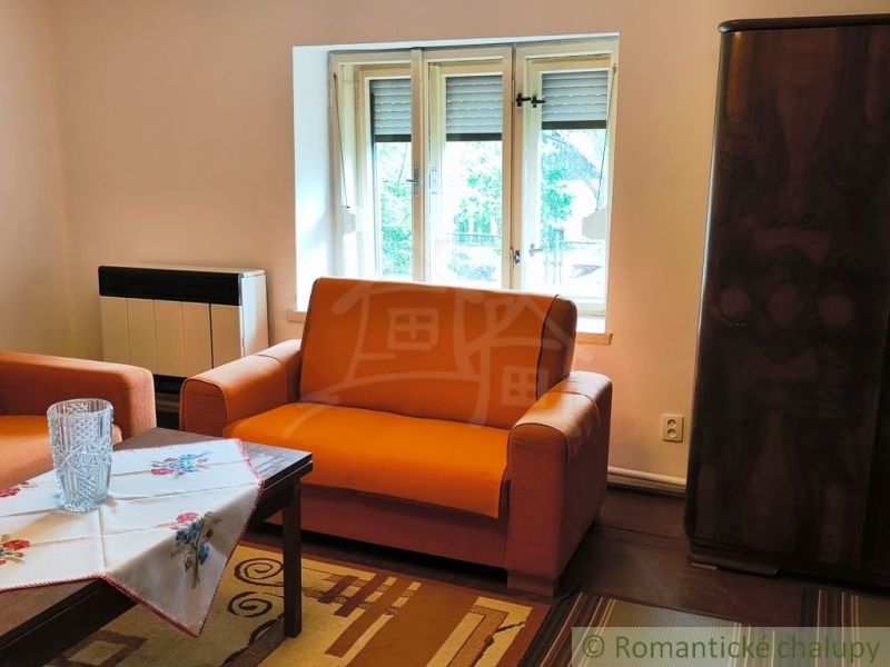 A cottage with an orange sofa set, wooden decor, and an embroidered tablecloth.