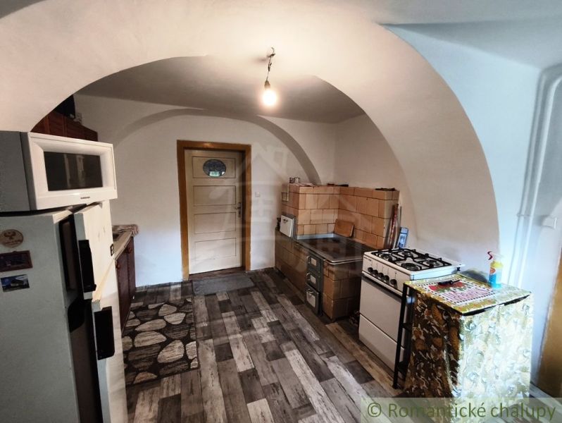 A kitchen in a cottage with a tiled stove and a floor with a wooden decor.