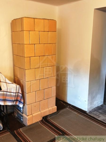 Tiled stove in the interior of a cabin with a wooden decor floor and woven rugs.
