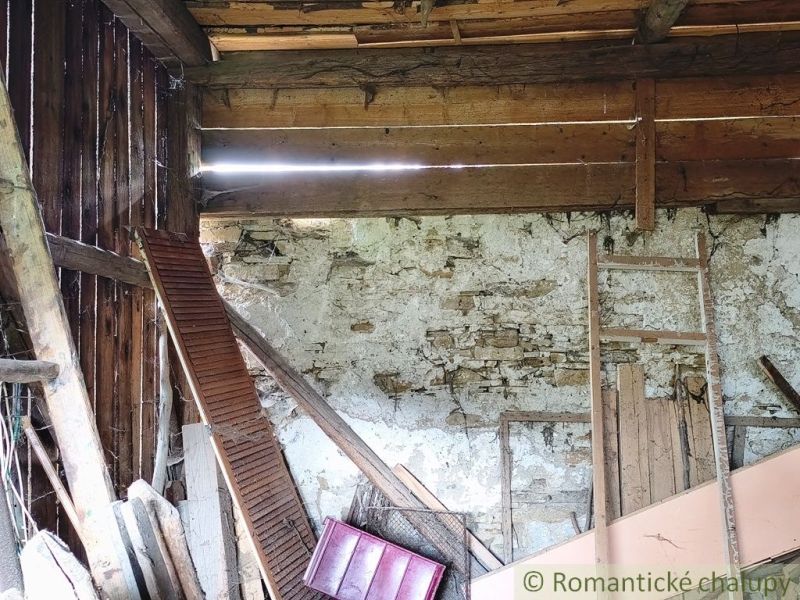Interior of a cottage with a stone wall and wooden beams, suitable for renovation.