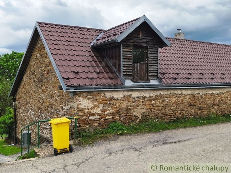 A stone cottage in Hermanovce with a metal roof and a yellow waste container.