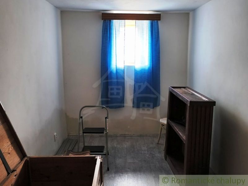 A room in a cottage with a blue curtain, stairs, and a floor with a wooden decor.