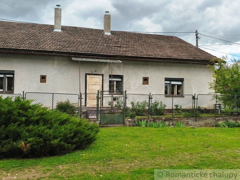 A cottage in Hermanovce with a garden, a fence, and an older facade, under a cloudy sky.