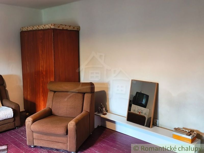In the interior of the cottage, there is a brown armchair, a wardrobe, and a mirror.