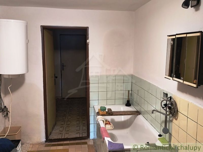 A bathroom in a cottage with a bathtub, tiles, and an electric boiler.