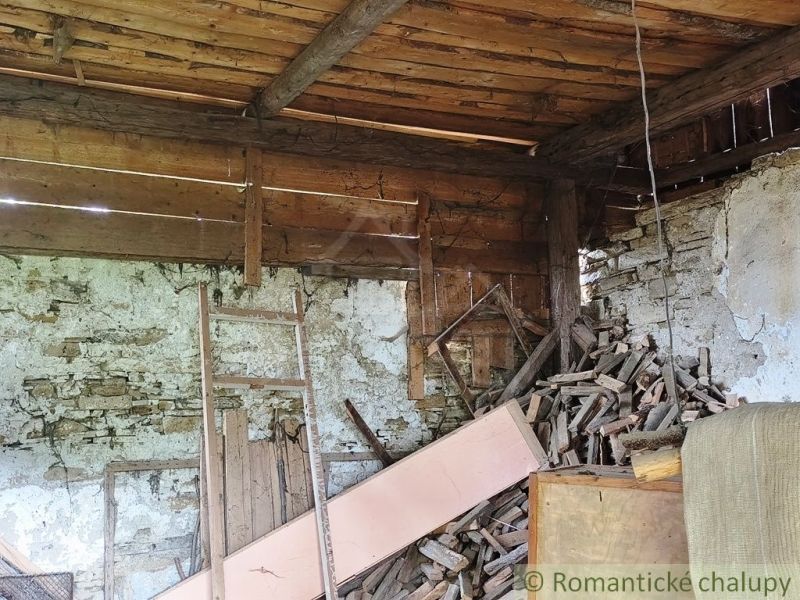 A wooden interior of a cabin with decaying boards and a stack of wood.