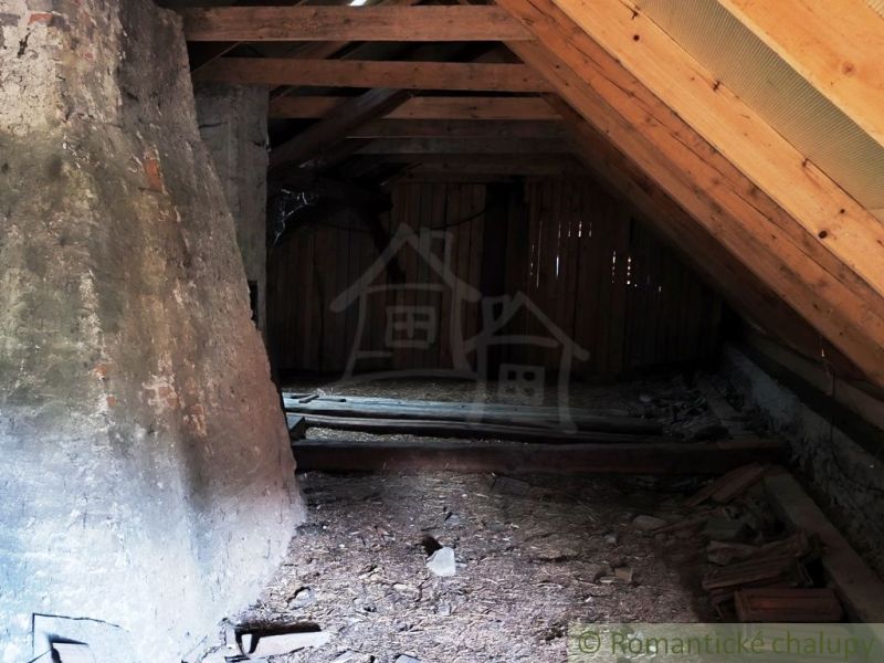 The attic in a wooden cabin with a beamed ceiling and a stone wall.