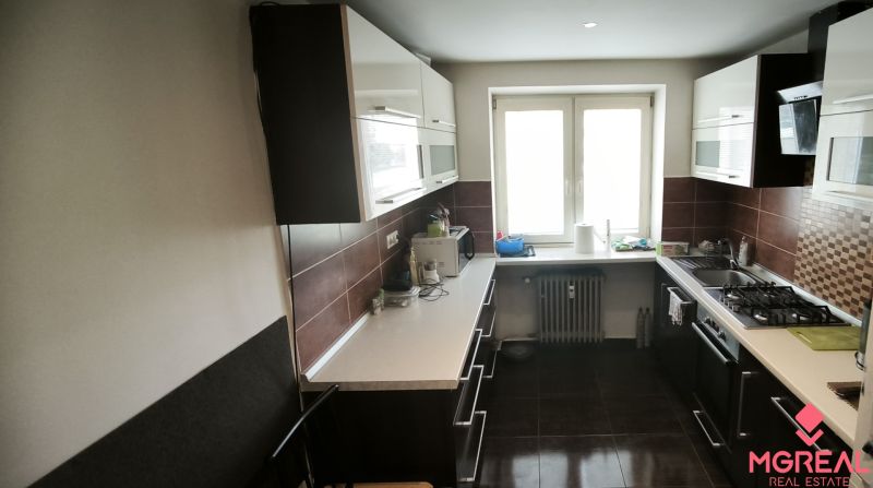 A kitchen with dark furniture, a white countertop, and a tiled floor in a 3-room apartment.