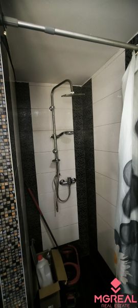 A shower corner in a 3-room apartment with black and white tiles and a shower curtain rod.