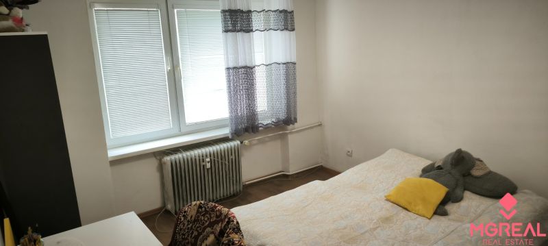 Bedroom in a 3-room apartment with a bed and a radiator, floor with wooden decor.