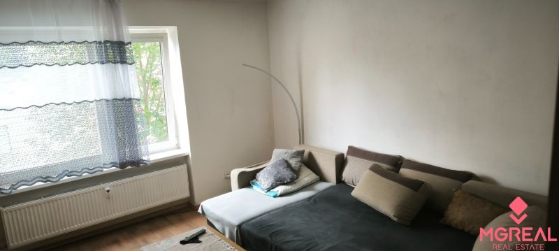 Living room in a 3-room apartment with a sofa, window, and wooden decor flooring.