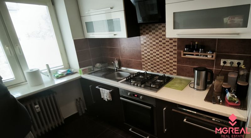 A kitchen in a 3-room apartment with a stove and a sink, surrounded by dark brown tiles.