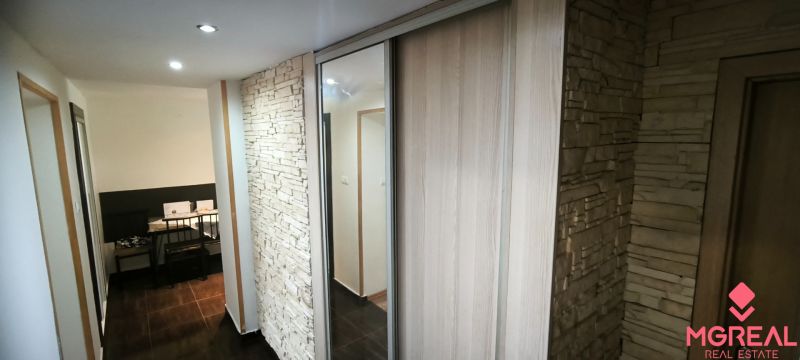 A hallway with stone cladding and a mirrored wardrobe in a 3-room apartment.