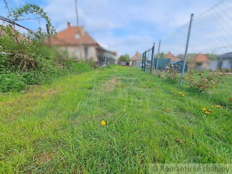 Gardens in Hruboňovo with thick grass, a fence, and a house in the background.
