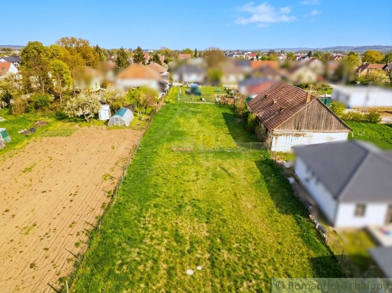 Gardens in Hruboňovo with a lawn, house, and field in the background.