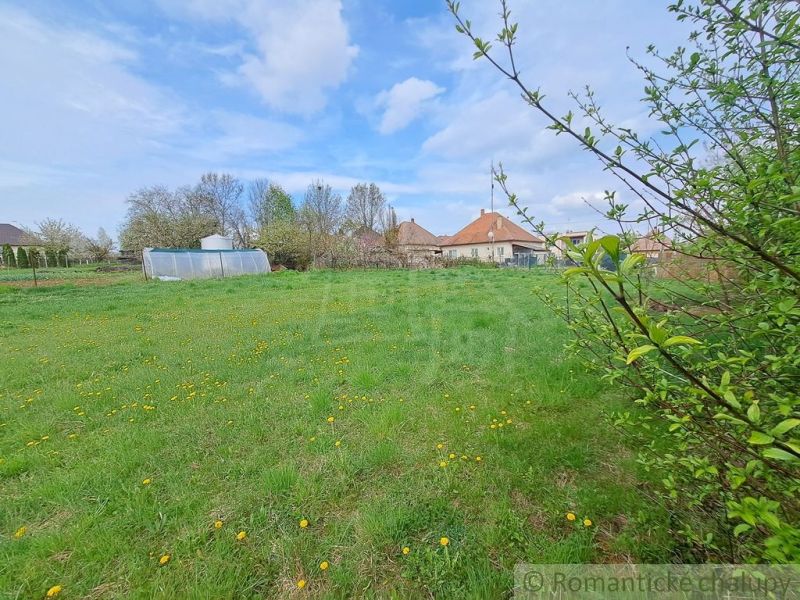 Gardens in Hruboňovo with a lawn and a greenhouse under the blue sky.
