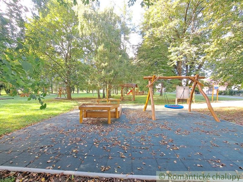 A playground with a slide and swings in the gardens of Hruboňovo, surrounded by greenery.