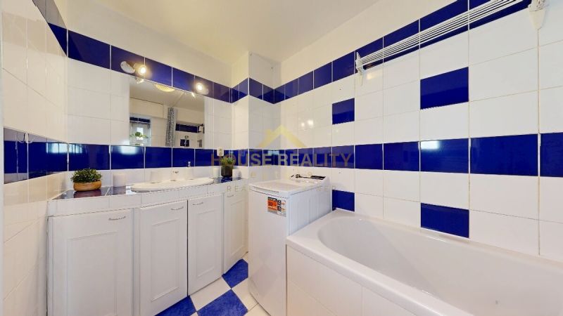 A bathroom in a studio apartment with white and blue tiles, a bathtub, and a washing machine.