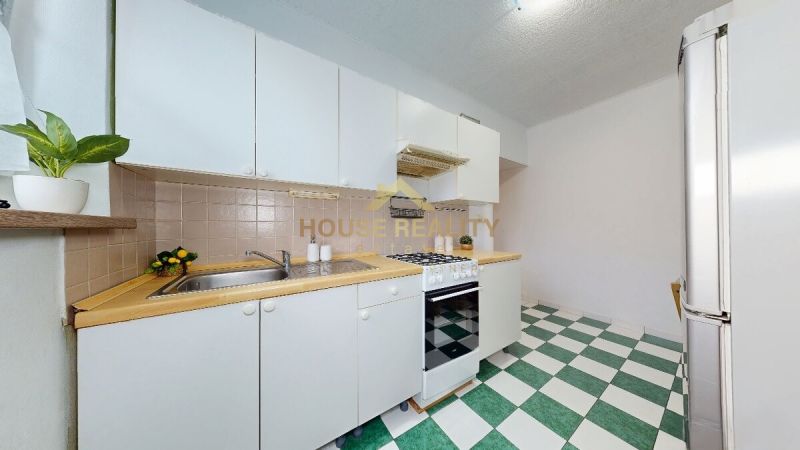 Kitchen in a one-room apartment with white cabinets and green and white tiles.