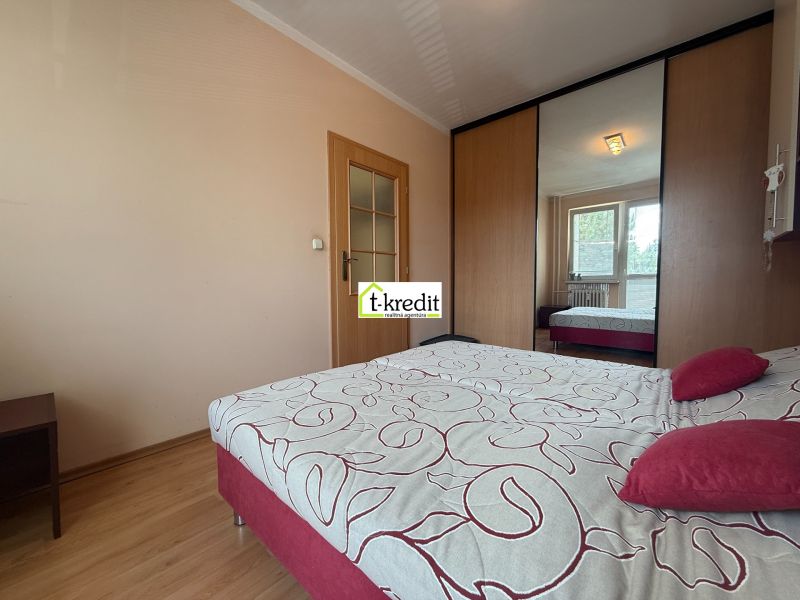 A bedroom with white walls, a wooden decor floor, a wardrobe, and a large bed.