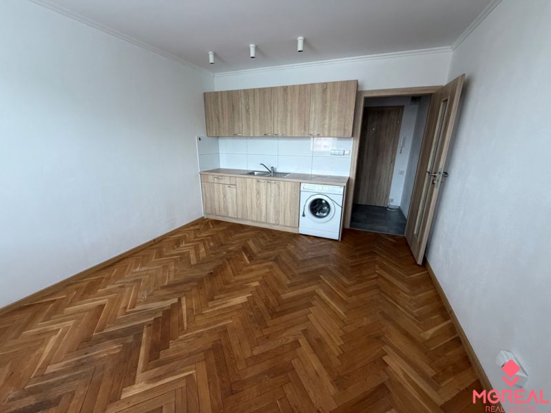 Studio apartment with a kitchenette, washing machine, and wooden decor flooring.