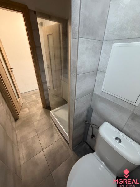 A studio apartment bathroom with a toilet and a shower, tiled with tiles.
