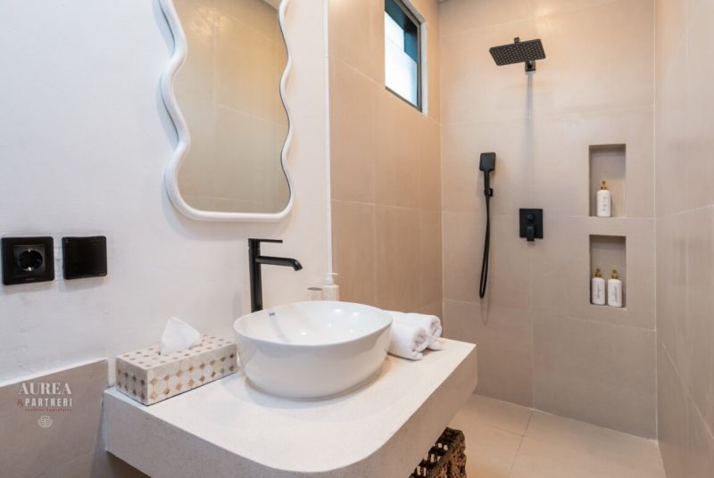 Bathroom in the villa with a countertop sink, mirror, and shower with black accessories.