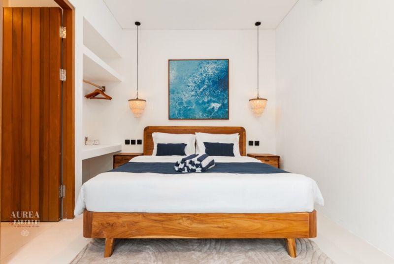 Bedroom with a wooden bed, pendant lamps, and a blue painting in a villa room.