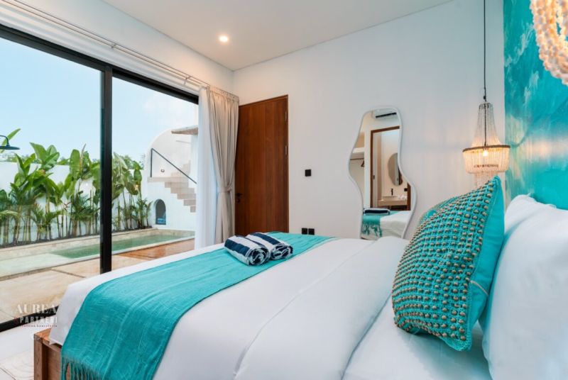 A bedroom in a villa with a pool, turquoise accessories, and large glass doors.