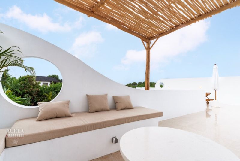 A terrace in a villa in Bali with white walls, an umbrella, and a wooden ceiling.