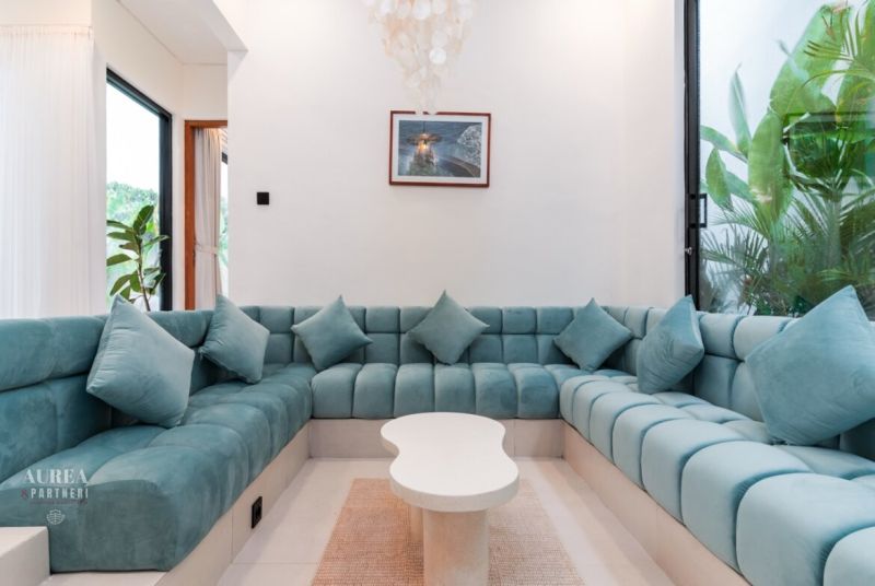 A comfortable blue couch in the interior of a villa with windows and plants.