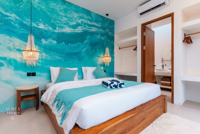 Bedroom in a villa with a turquoise wall, a comfortable bed, and atmospheric lights.