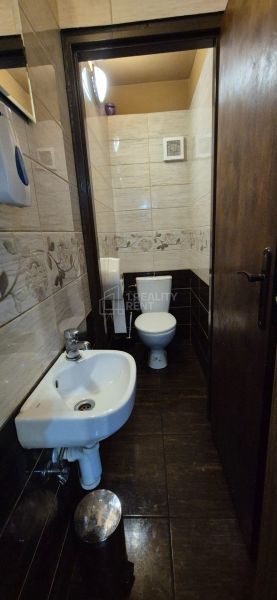 Bathroom in commercial premises with a toilet, sink, and tiles with a floral pattern.