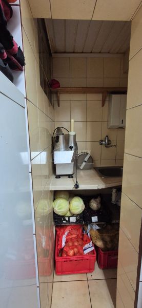 A narrow kitchenette in commercial premises with vegetables and a stainless steel sink.