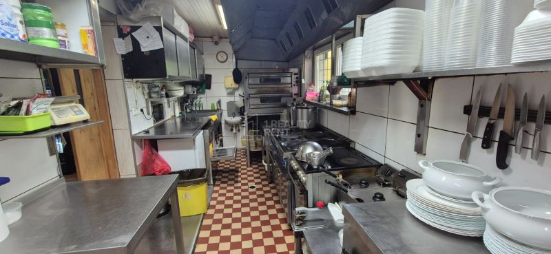 A kitchen in commercial premises with stainless steel counters, stoves, and shelves with dishes.