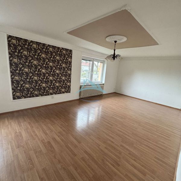 Spacious room with wood-patterned flooring and decorative wallpaper in a family house.