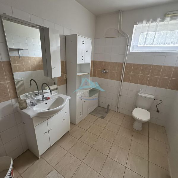 A bathroom in a family house with a sink and toilet, neutral tiles.