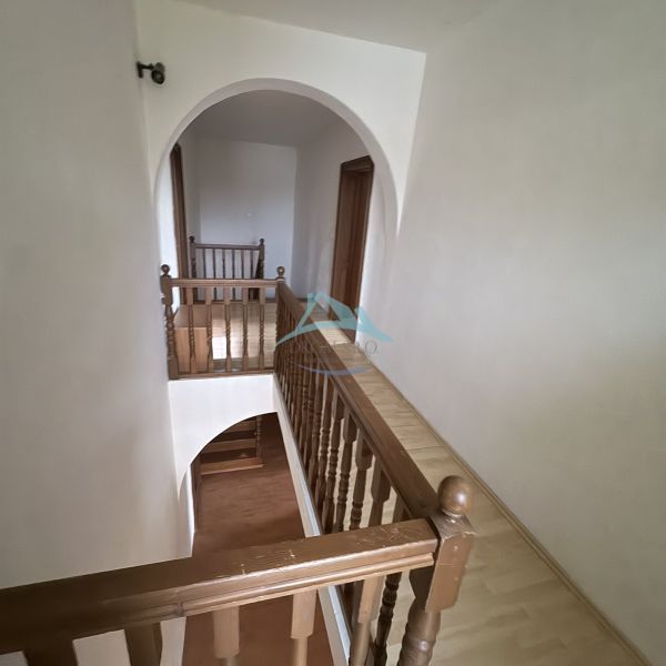 A hallway with an arch and wooden railing in a family house with a wood-patterned floor.