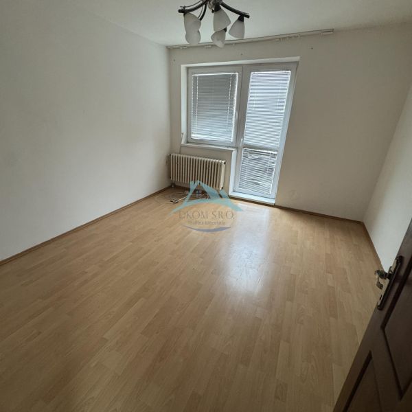 An empty room with a wood-patterned floor and a radiator in a family house.