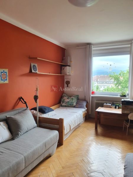 A room in a 3-room apartment with an orange wall and a wooden decor floor.