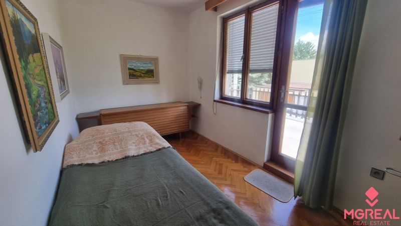 A bedroom in a family house with wooden decor and a large window.